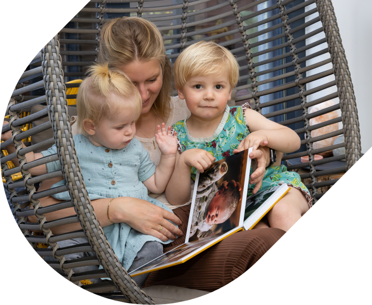 Draagmoeder in een hangstoel bekijkt een fotoboek met twee kinderen.